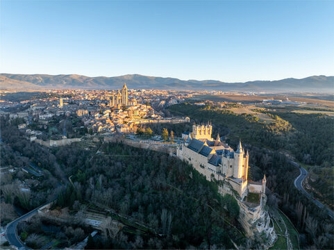 Aerial view of the Alc&Atilde;&iexcl;zar of Segovia rising majestically from a sea of green trees, framed by the ancient city and distant mountains in the golden light., Segovia, Castilla y Le&Atilde;&sup3;n, Spain.
