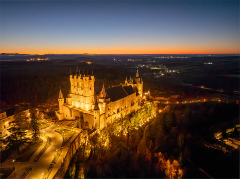 Aerial view of the Alc&Atilde;&iexcl;zar of Segovia glows warmly against the deep blue twilight sky, a medieval fortress perched majestically on a rocky crag, Segovia, Castilla y Le&Atilde;&sup3;n, Spain.