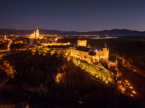 Aerial view of Alc&Atilde;&iexcl;zar of Segovia standing illuminated against the dark sky, with the city lights twinkling in the distance, Segovia Cathedral towering above, Segovia, Castilla y Le&Atilde;&sup3;n, Spain.