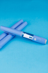 Vertical. Overhead shot of semaglutide pens on bright blue table, symbolizing wellness, healthcare...