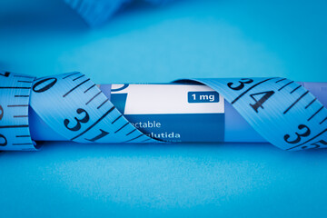 Closeup of semaglutide pens coiled with blue tape measure on vibrant blue surface, symbolizing...