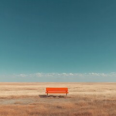 Obraz premium Lone orange park bench sits in a vast empty field under a clear blue sky