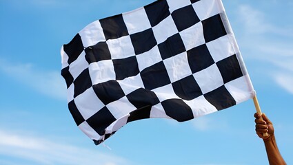 Checkered flag waving against a clear blue sky, held by a hand in a gesture of victory.