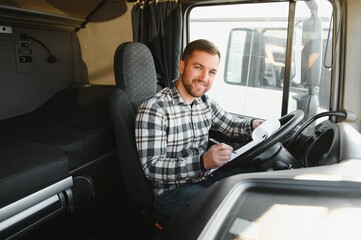 Truck driver is sitting behind the wheel holding a clipboard and checking the documents for the...