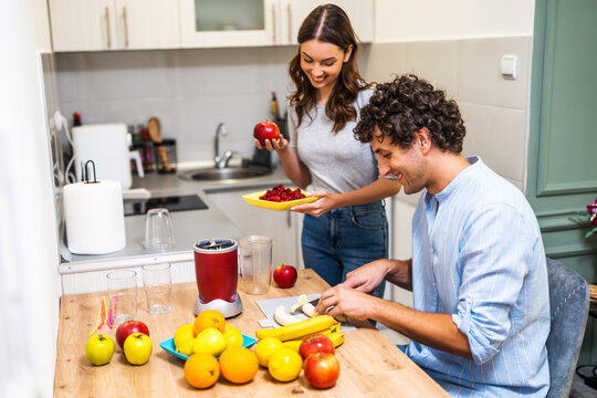Adult couple is preparing smoothie in their kitchen. They have various fruits ready to be mixed in electric juicer. - Powered by Adobe