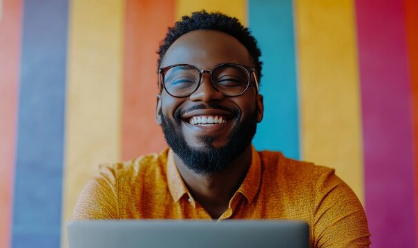 Happy gay black man working on a laptop. Smiling African American remote worker laughing on a video call with team colleagues. Pride Month banner featuring a rainbow flag, Generative AI
