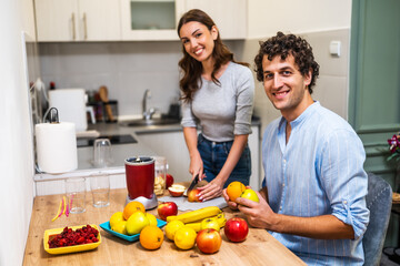 Adult couple is preparing smoothie in their kitchen. They have various fruits ready to be mixed in electric juicer.
