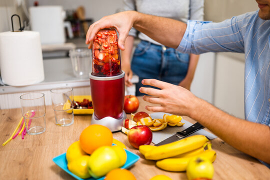 Close up of adult couple preparing smoothie in their kitchen. They are mixing various fruits in electric juicer. - Powered by Adobe