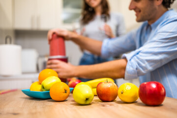 Close up of adult couple preparing smoothie in their kitchen. They are mixing various fruits in electric juicer.