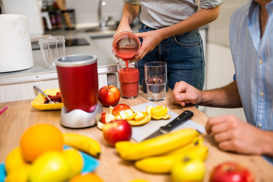 Close up of adult couple preparing smoothie in their kitchen. They are mixing various fruits in electric juicer.