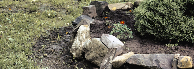 ​A flower bed with various plants and decorative bushes next to a metal fence. Small pink and...