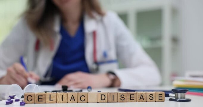 Wooden cubes spell Celiac Disease put near pills and stethoscope on table. Light enters room creating place while doctor studies gluten free therapy