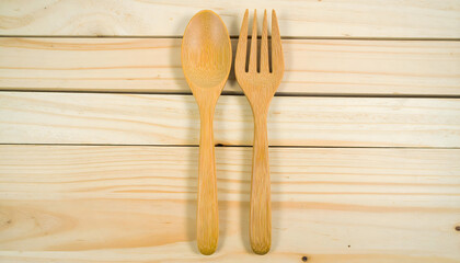 Rustic wooden spoon and fork neatly placed side by side on a light-colored wooden table, ready for a natural dining experience or as kitchen utensils.