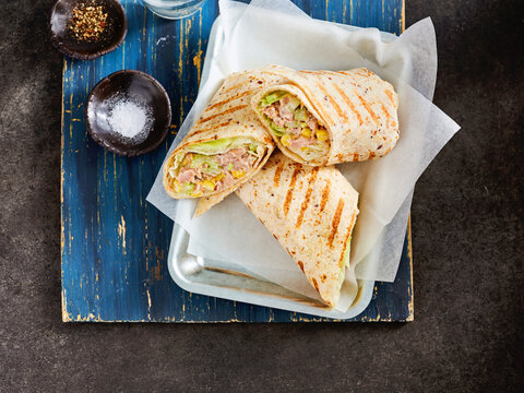 A delicious tuna wrap showcases tender chunks of tuna mixed with fresh vegetables, all wrapped in a soft tortilla. Served on a rustic wooden platter with salt and spices