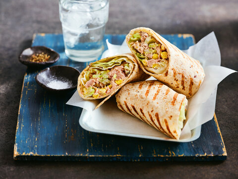 Freshly made tuna wraps filled with crisp vegetables are presented on a plate, accompanied by a glass of water and spices. This dish highlights nutritious ingredients perfect for a light meal