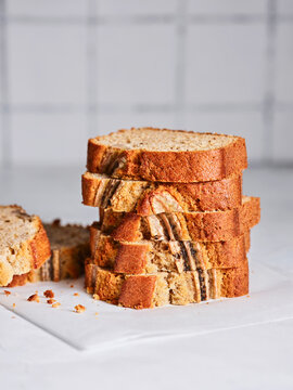 Freshly baked banana bread is sliced and neatly stacked on a white surface, showcasing its inviting texture and delightful aroma, perfect for a breakfast treat or snack