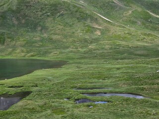 La Thuile, Val D'Aosta, July 02 2025: Panoramic view to the alps, beautiful green landscape reflected in a small natural lake. Beautiful blue sky with some clouds. Mountains with a little snow. Aerial