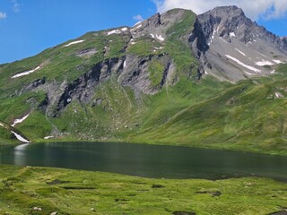 La Thuile, Val D'Aosta, July 02 2025: Panoramic view to the alps, beautiful green landscape reflected in a small natural lake. Beautiful blue sky with some clouds. Mountains with a little snow. Aerial