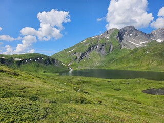 La Thuile, Val D'Aosta, July 02 2025: Panoramic view to the alps, beautiful green landscape reflected in a small natural lake. Beautiful blue sky with some clouds. Mountains with a little snow. Aerial