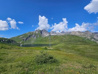 La Thuile, Val D'Aosta, July 02 2025: Panoramic view to the alps, beautiful green landscape reflected in a small natural lake. Beautiful blue sky with some clouds. Mountains with a little snow. Aerial