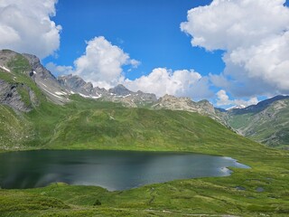La Thuile, Val D'Aosta, July 02 2025: Panoramic view to the alps, beautiful green landscape reflected in a small natural lake. Beautiful blue sky with some clouds. Mountains with a little snow. Aerial