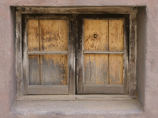 old, weathered window with wooden shutters, the window is set into a wall, which also has a rough,...
