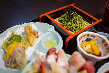 Cold green tea soba noodles topped with seaweed, served with vegetable tempura and side dishes as...