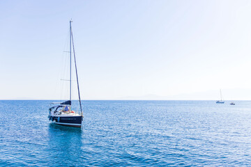 Fototapeta premium Beautiful summer seascape with a sailing yacht and a small motorboat floating on crystal-clear turquoise water. A sunlit island can be seen in the distance, under a cloudless blue sky. The peaceful