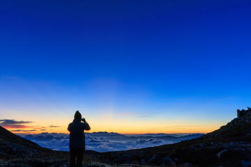 雲海と夜明け前の空を撮影する登山者のシルエット