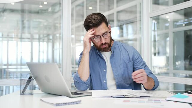 Businessman is tired of doing paperwork and doing tasks sitting at workplace in business office. Confused businessman having difficulty with work on documents. Exhausted male worker procrastinates