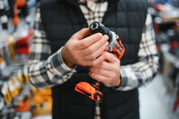Portrait of young bearded man buying modern electric drill while standing in tool. Hardware construction site objects concept