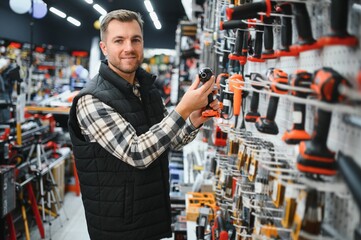 man holding and choosing electric screwdriver, standing in construction store