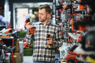 man holding and choosing electric screwdriver, standing in construction store