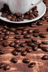 Roasted coffee beans on a wooden surface close to a coffee cup.