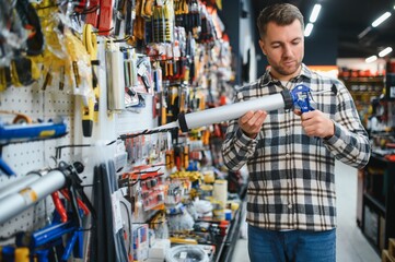 A male customer in a modern hardware store chooses a silicone gun