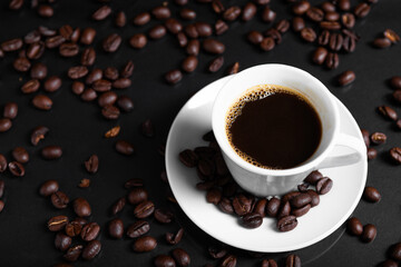 A espresso cup filled with dark coffee surrounded by roasted beans on reflective surface.