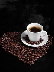 Espresso cup on a black background with roasted coffee beans in the shape of a heart.