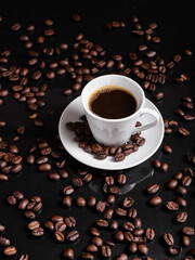 A espresso cup filled with dark coffee surrounded by roasted beans on reflective surface.