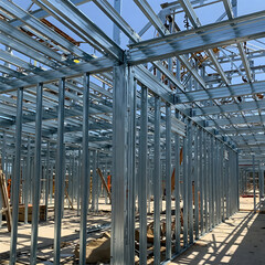 Fototapeta premium The interior metal framing of a building under construction, showing vertical studs, horizontal tracks, and roof trusses against a bright sky. Generative AI.