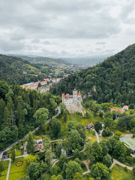 Aerial view of Bran Castle's terracotta rooftops piercing through the lush green canopy, nestled serenely in the valley under a subdued sky, Bran, Jude&Egrave;&rsaquo;ul Bra&Egrave;&trade;ov, Romania.