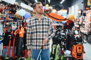 happy customer with electric lawn trimmer in hands at garden equipment store