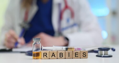 Lady doctor writes at desk with Rabies on wooden blocks and vial with syringe. Serious viral disease of rabies highlights importance of vaccination
