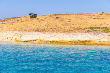 A tranquil scene featuring a crystal-clear turquoise sea gently lapping against a dry, rocky coastline under a cloudless blue sky. This peaceful landscape evokes the essence of summer and natural