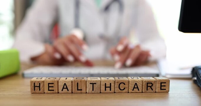 Female professional uses keyboard near Healthcare on wooden blocks on desk. Medical industry and essential services provided in healthcare sector
