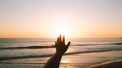 Hand reaching towards the sun on a beach during a bright colorful sunset