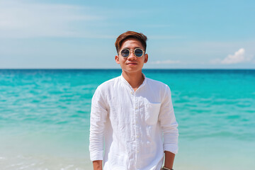 Man in white linen shirt stands on beach with turquoise water and clear sky