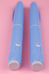 Vertical, Overhead shot of semaglutide pens on vibrant pink table, symbolizing weight loss, healthcare technology, and patient support.