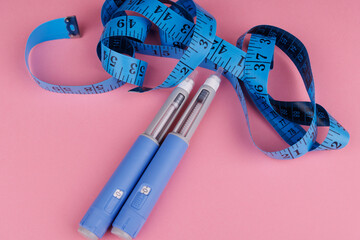 Top view of semaglutide pens coiled with tape on pink surface, symbolizing patient care, weight...