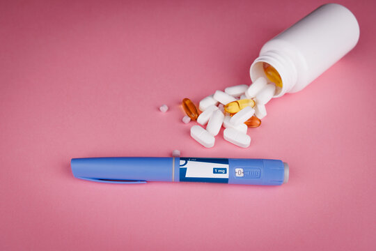 Top view of semaglutide pens with blue tape and white pill bottle on pink table, pills scattered, symbolizing wellness, telehealth, and patient care.