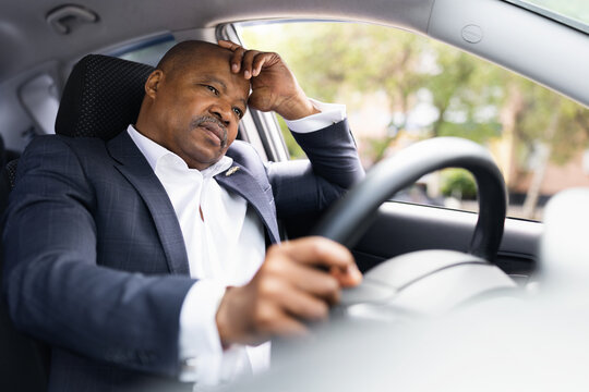 Stressed African American businessman driving car looking tired. Concept of fatigue, stress, travel exhaustion and corporate lifestyle under pressure